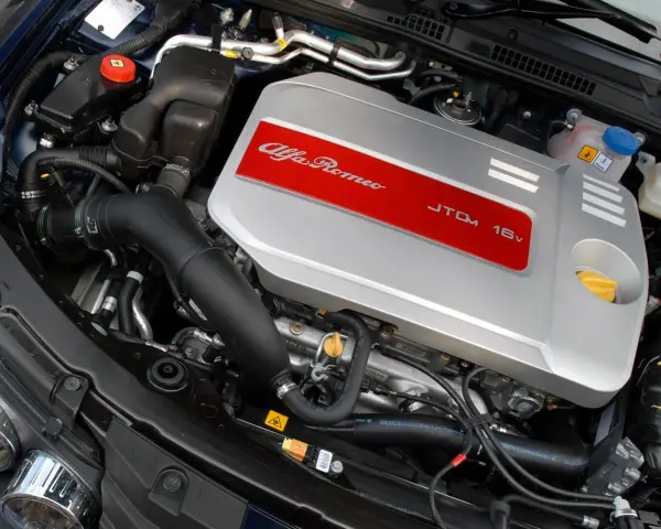 Silnik Alfa Romeo 1.9 JTD 16V z widocznym srebrnym deklom z czerwonym pasem i napisem.