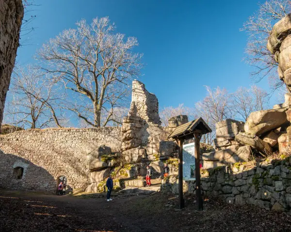 Ruiny zamku na rudawach janowickich. Kamienne mury, skalne formacje i nagie drzewa pod błękitnym niebem.