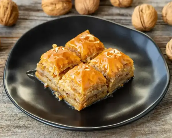 Słodka baklawa na czarnym talerzu, idealna do domowego przepisu. Orzechy włoskie w tle.
