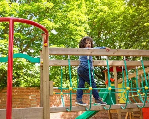 Chłopiec na placu zabaw, wesoły park rysunek. Dziecko wspina się po drewnianej konstrukcji z zielonymi linami.