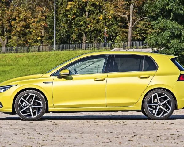 Żółty hatchback Volkswagen Golf VIII z przyciemnianymi szybami stoi na tle zieleni i drzew.