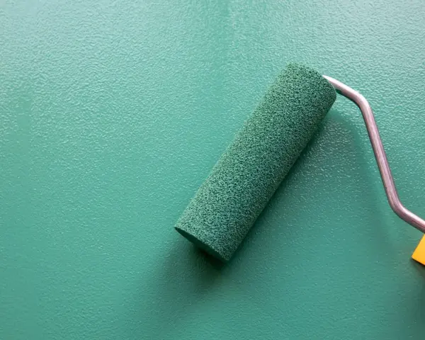 Rodillo de pintura verde sobre pared texturizada. Se puede pintar sobre papel pintado para renovar espacios.
