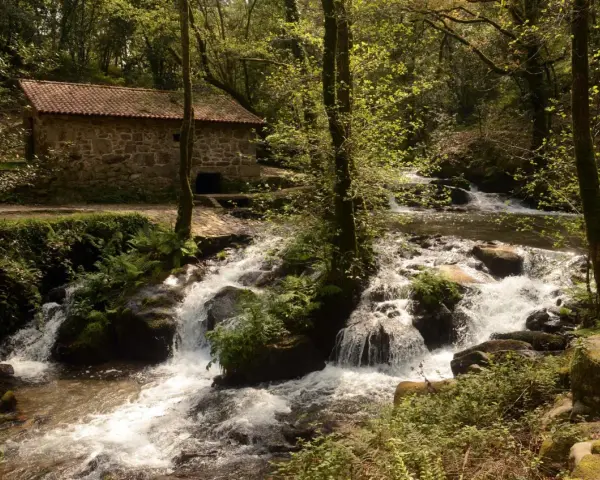 Antigua casa de piedra junto a un río con cascadas, ideal para una ruta senderismo Vigo.