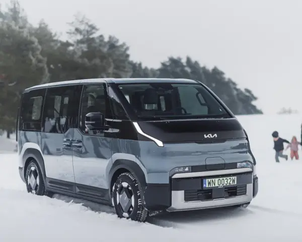 Szary elektryczny minivan Kia EV9 na śniegu, z rodziną w tle.