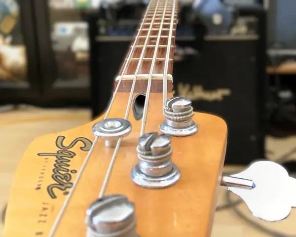 Nahaufnahme des Bass-Kopfes mit Saiten und Stimmmechaniken. Der Schriftzug "Squier by Fender Jazz Bass" ist sichtbar. Perfekt, um den Bass einzustellen.