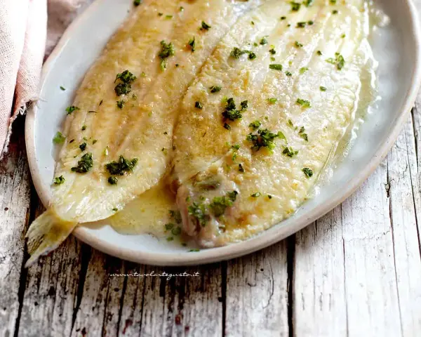 Sogliola alla mugnaia dorata e succulenta, cosparsa di prezzemolo fresco, servita su un piatto ovale.