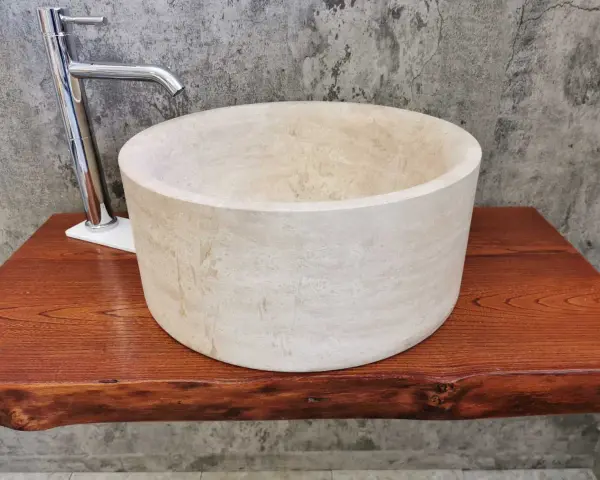 Lavabo cilindrico in pietra naturale chiara, con rubinetto cromato, su un piano in legno grezzo. Un esempio di come i nomi delle pietre naturali si trasformano in design unici.