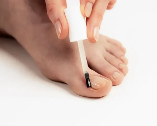 Application d'un soin transparent sur un ongle abîmé pour le protéger et le renforcer.