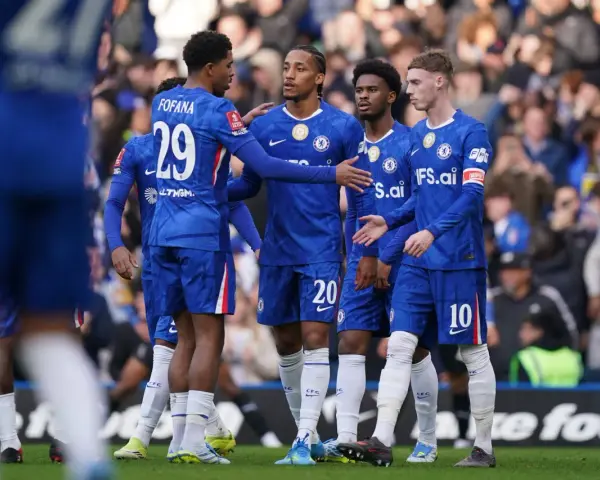 Piłkarze Chelsea w niebieskich strojach rozmawiają na boisku. Widać numery 29, 20 i 10.