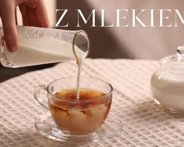 Ręka wlewa mleko do szklanki z herbatą, tworząc piękne smugi. Obok stoi cukiernica. Idealna herbata z mlekiem na chłodny dzień.