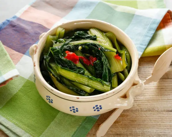 Cicoria in padella, un contorno saporito con peperoncino, servita in una ciotola decorata su un tagliere di legno.
