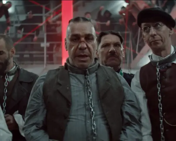 Rammstein - Deutschland: mężczyźni w łańcuchach, w tle czerwone światła i ludzie na schodach.