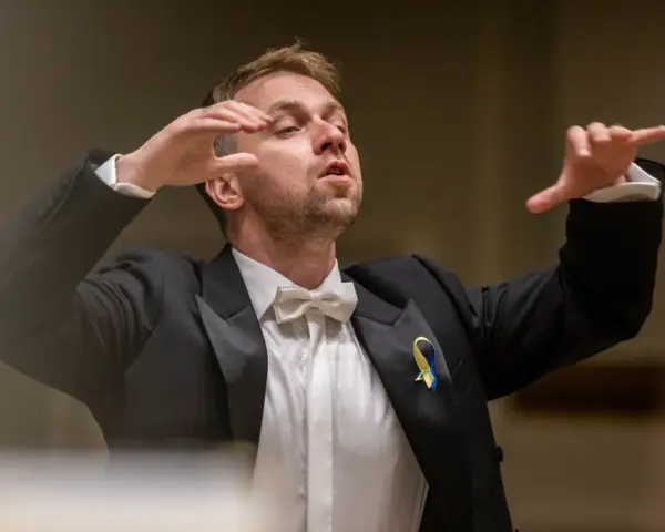 Dyrygent w garniturze z kokardką, prowadzący wykonanie Carmina Burana, z ukraińską wstążką na klapie.