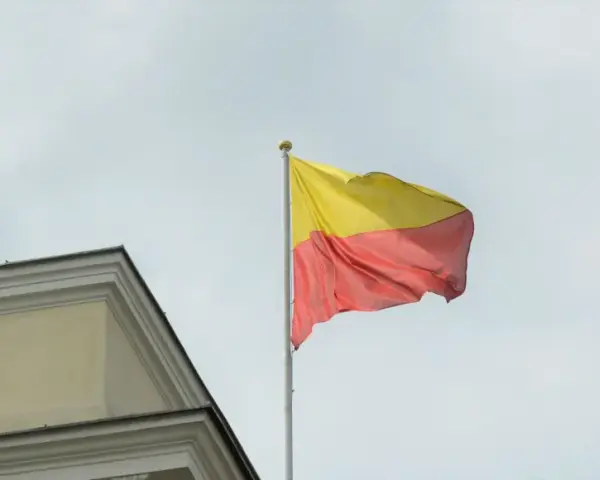 Flaga Łotwy z żółtym i czerwonym pasem, powiewająca na maszcie obok budynku.