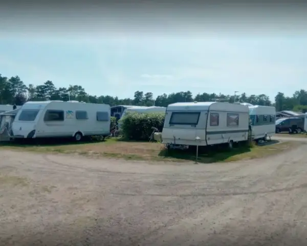 Ställplatser med husvagnar och bilar på Olles camping. Träd och blå himmel syns i bakgrunden.