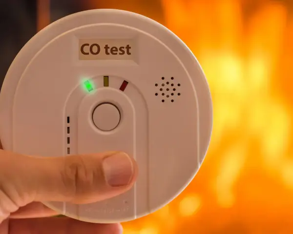 Detektor czadu z zieloną diodą i napisem "CO test" na tle płomieni.