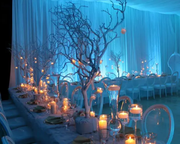 A long table set for an event with white chairs, candles, and white tree branches decorated with small lights.