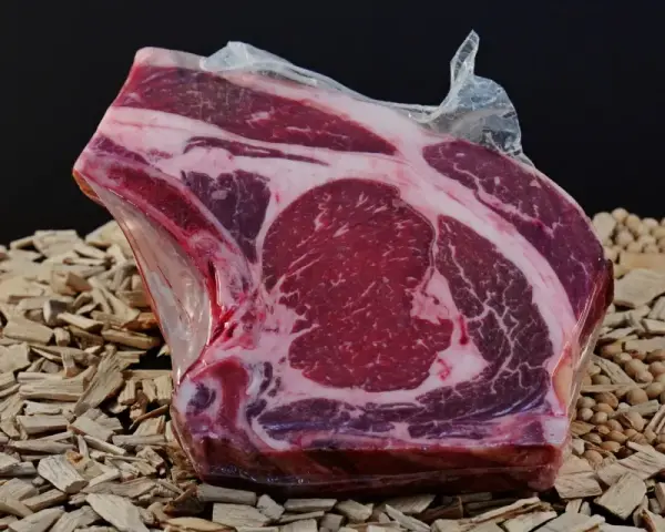 A vacuum-sealed raw beef steak with marbling sits on a bed of wood chips and small nuts.