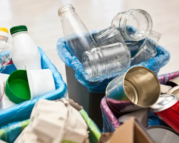 Segregacja odpadów: szklane słoiki, plastikowe butelki i puszki czekają na wywóz śmieci.