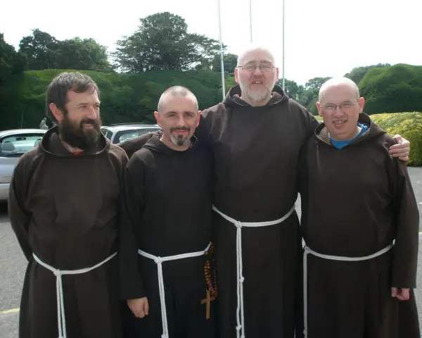 Four monk priests in brown robes stand together outdoors.