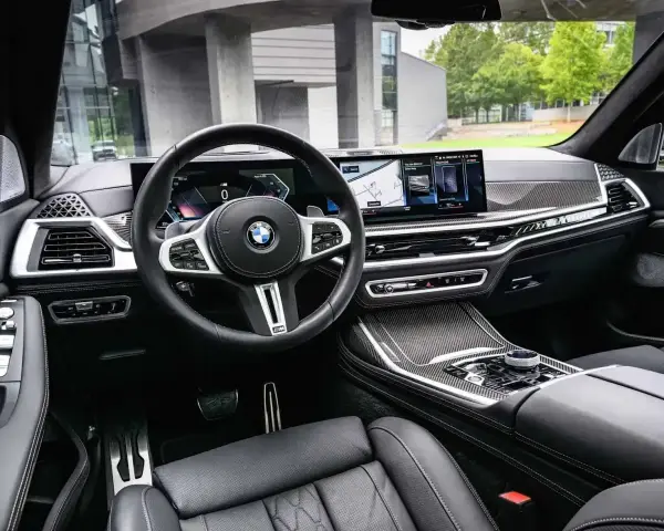 Wnętrze BMW x7: skórzana tapicerka, nowoczesny kokpit z dwoma ekranami i sportowa kierownica.