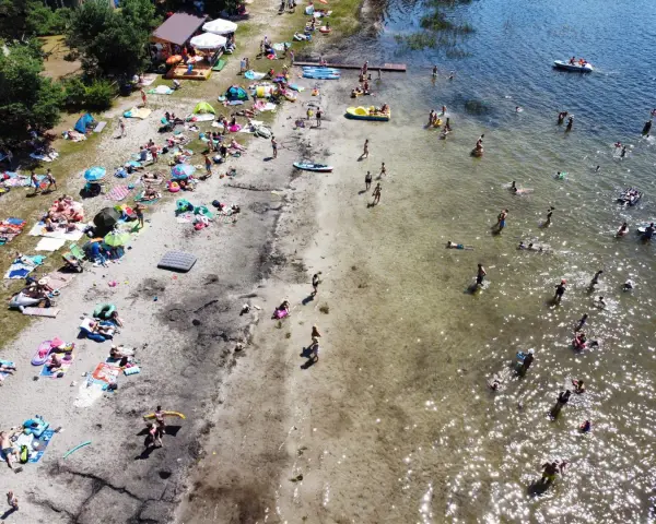 Tłoczna plaża nad jeziorem, ludzie opalają się, kąpią i pływają. Wakacyjny wypoczynek na **jeziorach lubelskich**.