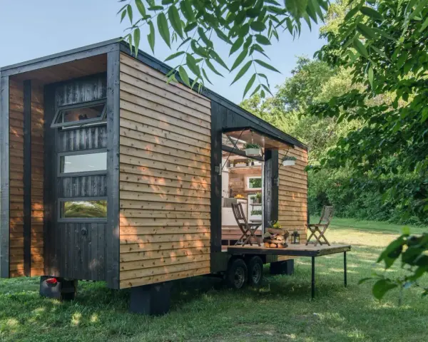 Casa móvil de madera en un terreno no urbanizable, con mesa desplegable y sillas.