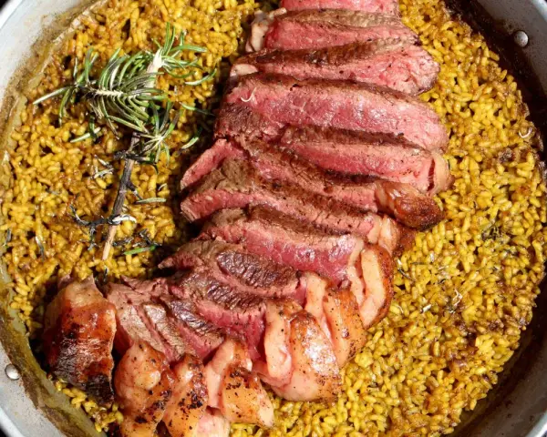 Arroz amarillo con chuletón a la parrilla y romero en paellera.