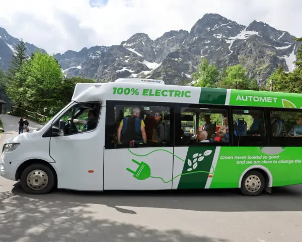 Elektryczny bus na Morskie Oko, z pasażerami w środku, na tle gór.