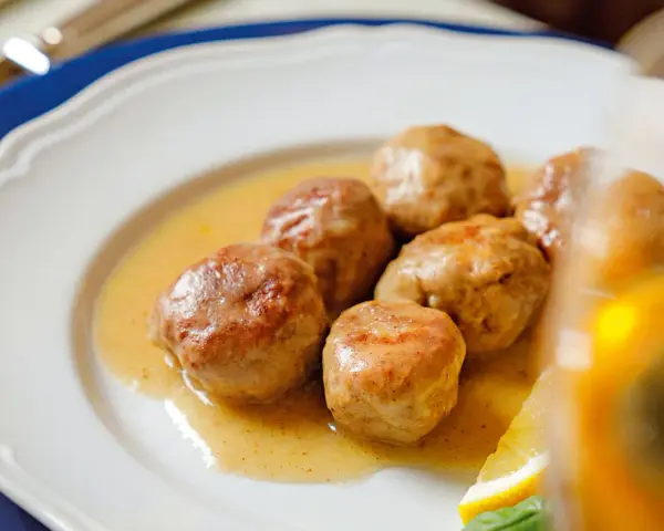 Polpette al limone succulente in un piatto bianco, con una fetta di limone e basilico.