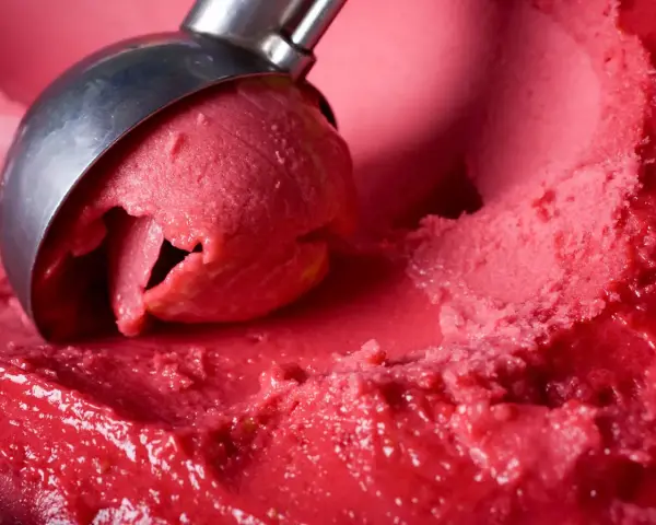 Ein Löffel nimmt eine Kugel leuchtend rotes Eis auf. Es sieht aus wie ein köstliches Blaubeereis, das zum Genießen bereit ist.