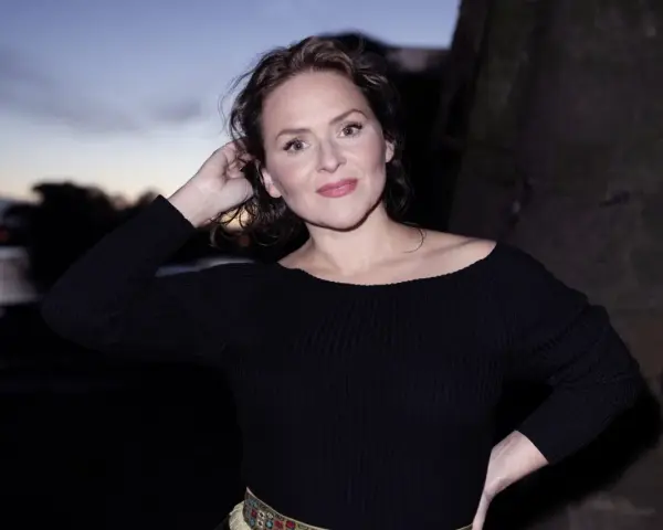 Emiliana Torrini, la chanteuse, pose au crépuscule près de l'eau, une main dans ses cheveux.