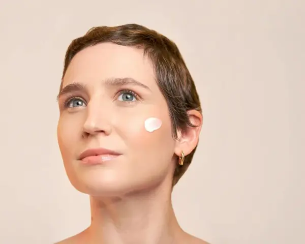 Une touche de crème solaire avant ou après crème hydratante sur la joue d'une femme au regard pensif.