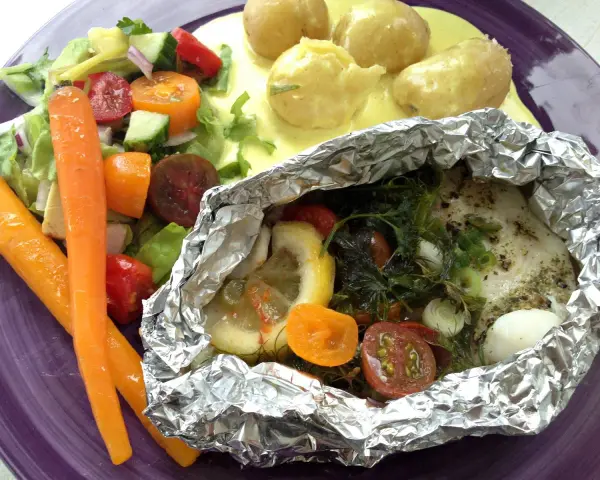 Torsk i foliepaket med citron och dill, serverad med färsk sallad, morötter och potatis i sås.
