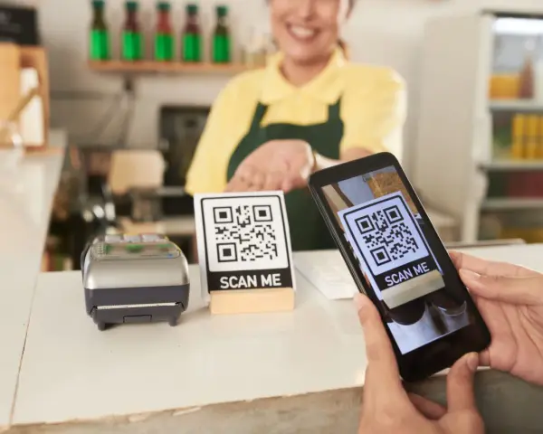 Cliente usa su móvil para escanear un código QR y hacer su carta digital. Un datáfono y otro código QR esperan en el mostrador.