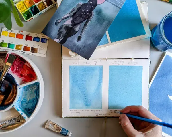 Paleta de acuarelas, pinceles y muestras de pintura azul. Un artista experimenta con técnicas de pintar acuarela.