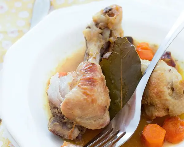 Delicioso pollo guisado con zanahorias y hoja de laurel en un plato blanco, listo para ser disfrutado.