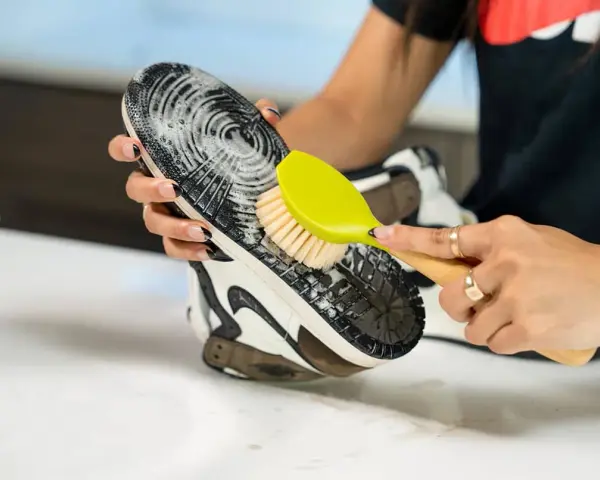 Mani che puliscono la suola di una scarpa con una spazzola gialla e schiuma. Un modo efficace per capire come pulire la suola delle scarpe.