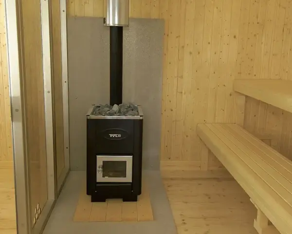 En nybyggd bastu utomhus med vedkamin, stenar och träbänkar. Perfekt för avkoppling.