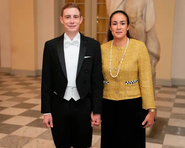 Jonas Vingegaard and his wife, Trine Marie, dressed formally for an event. He wears a tuxedo, and she sports a yellow tweed jacket and pearl necklace.