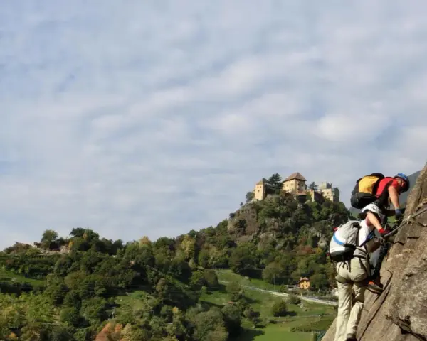 Zwei Kletterer am hoachwool Klettersteig mit Burg im Hintergrund.