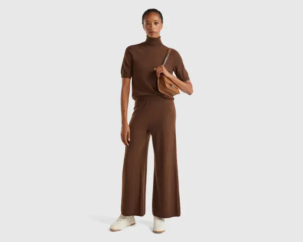 Mujer con conjunto marrón de cuello alto y pantalón ancho, bolso camel. Colores que combinan con el marrón, como el camel, resaltan la elegancia.