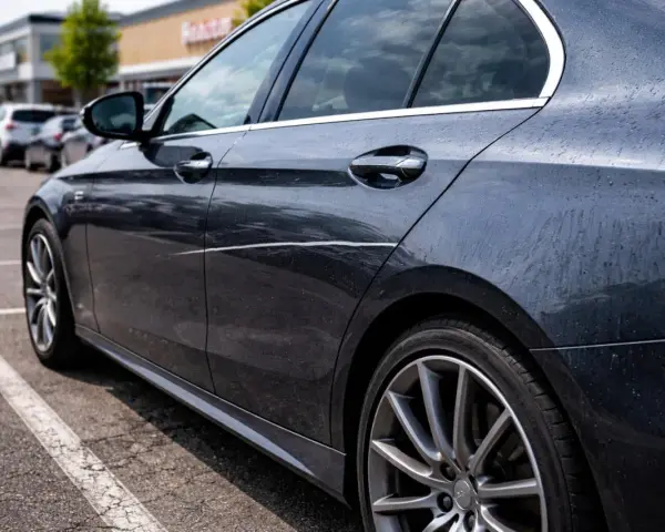 Ciemny samochód na parkingu z widocznym, długim, nieświadomym zarysowaniem na drzwiach.
