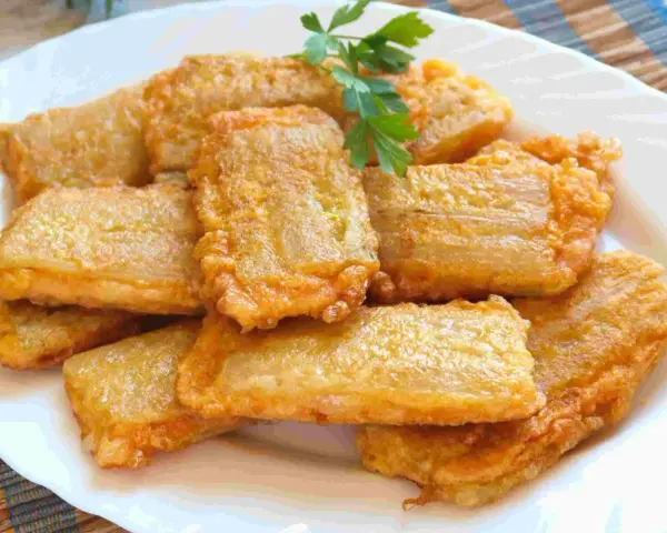 Pencas rellenas doradas y crujientes, apiladas en un plato blanco, con una ramita de perejil fresco.