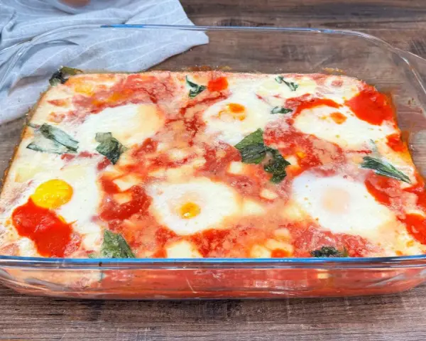 Uova alla contadina appena sfornate in teglia di vetro, con pomodoro e basilico.