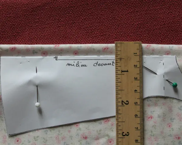 Patron de couture marqué "milieu devant", épinglé sur un tissu fleuri. Une règle en bois mesure la pièce.