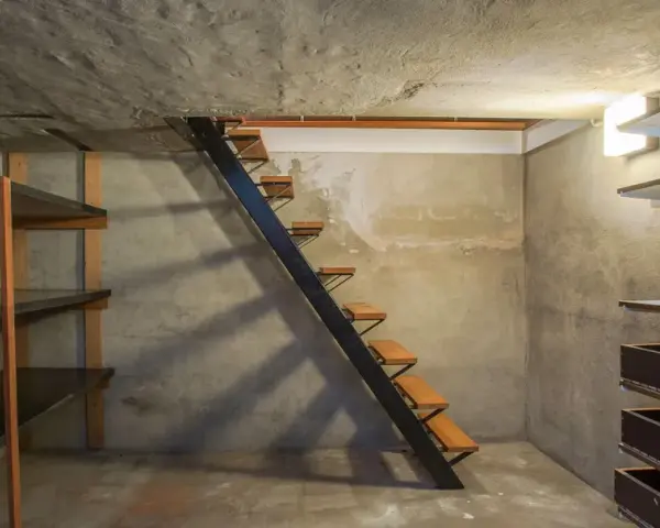Escaliers métalliques menant à une cave en cours d'aménagement, avec étagères brutes et murs en béton. Idéal pour creuser une cave sous sa maison.