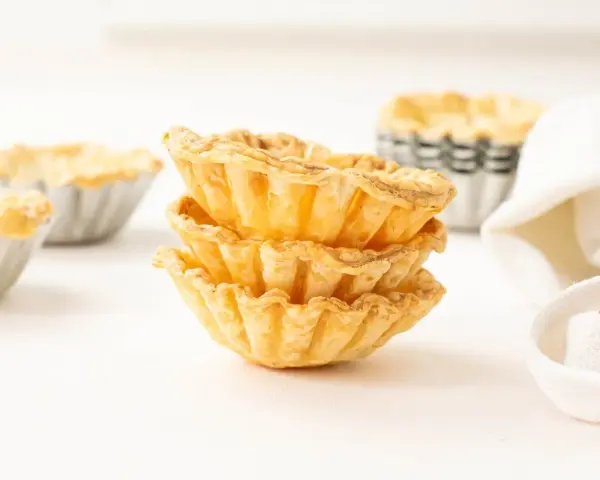 Montón de tartaletas de hojaldre listas para rellenar con crema pastelera.