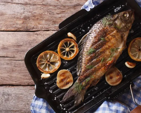Gegrillter Karpfen mit Zitronenscheiben und Kräutern auf einer Grillpfanne. Ein Genuss, Karpfen zu essen!