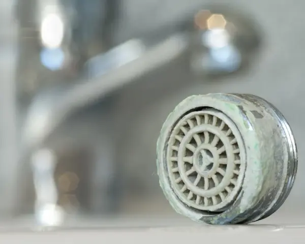 Zwapniony aerator kranu, który pokazuje, jak wyjąć sitko z kranu.